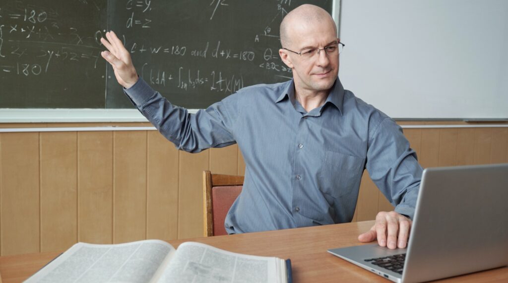 Teacher pointing at blackboard in front of laptop